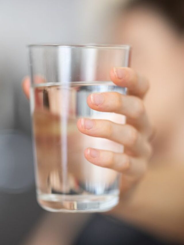 Mão segurando um copo de água limpa, representando a pureza da água filtrada por um purificador.