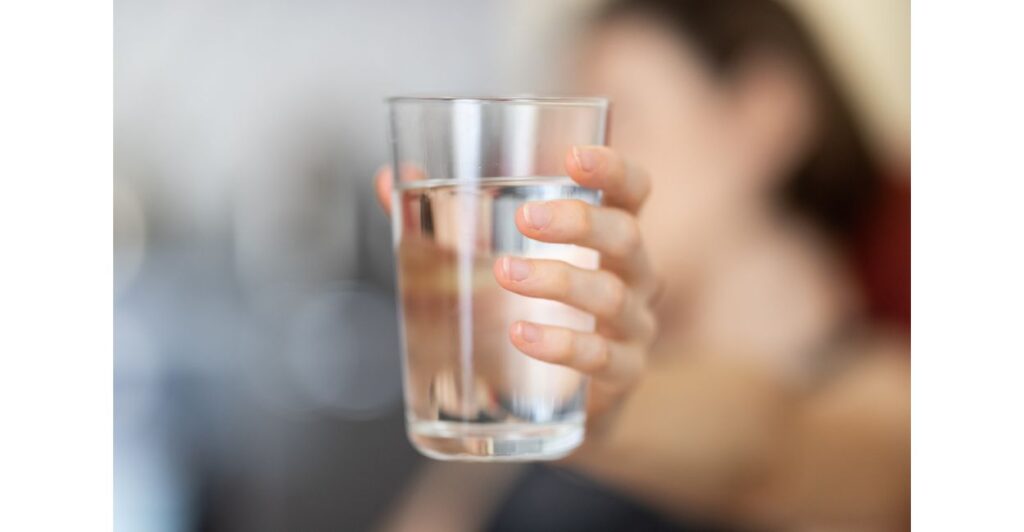 Mão segurando um copo de água limpa, representando a pureza da água filtrada por um purificador.