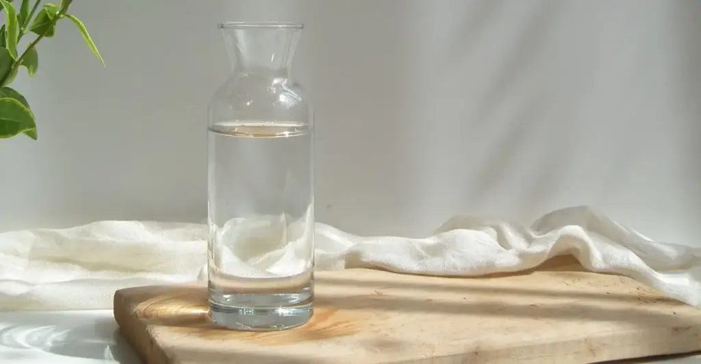 Jarra de água transparente com filtro de carvão ativado em cima de uma mesa de madeira, ilustrando purificação caseira de água.